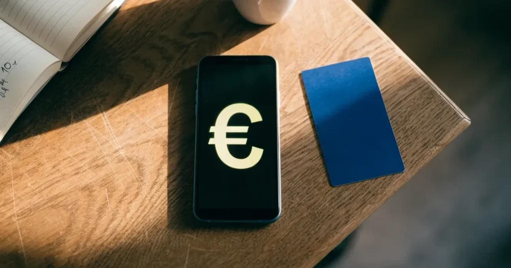 Uno smartphone e una carta di pagamento affiancati su un tavolo di legno, con alcune banconote da euro accanto