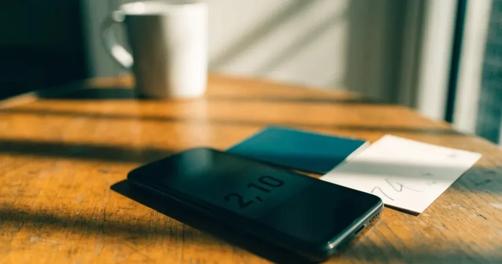 Uno smartphone e una carta di pagamento affiancati su un tavolo di legno, con alcune banconote da euro accanto
